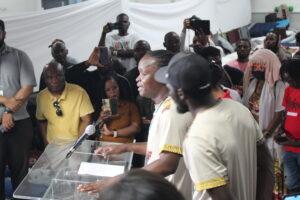 Christopher Lordson speaking behind a podium to cameras with a crowd behind him in Revivaltimes Tabernacle Church