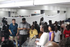 Pastor Judith standing beside Mayor Olivia Chow speaking behind a podium to cameras with a crowd behind her in Revivaltimes Tabernacle Church